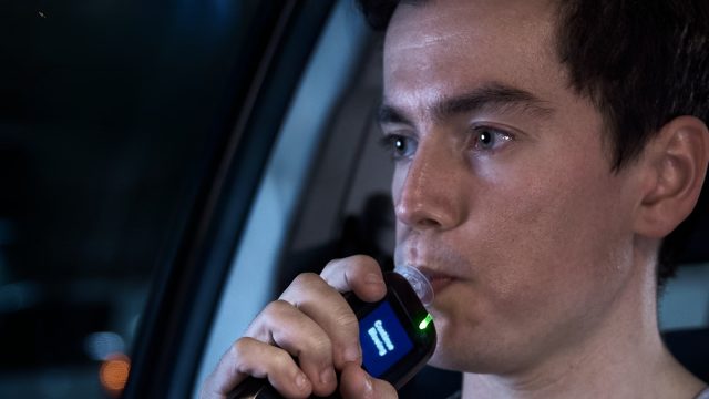 A young man doing a roadside breath test. Text on image says 'Harsh penalties for all drink drivers.'